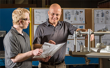 Two engineers reviewing technical drawings beside an industrial air knife setup.